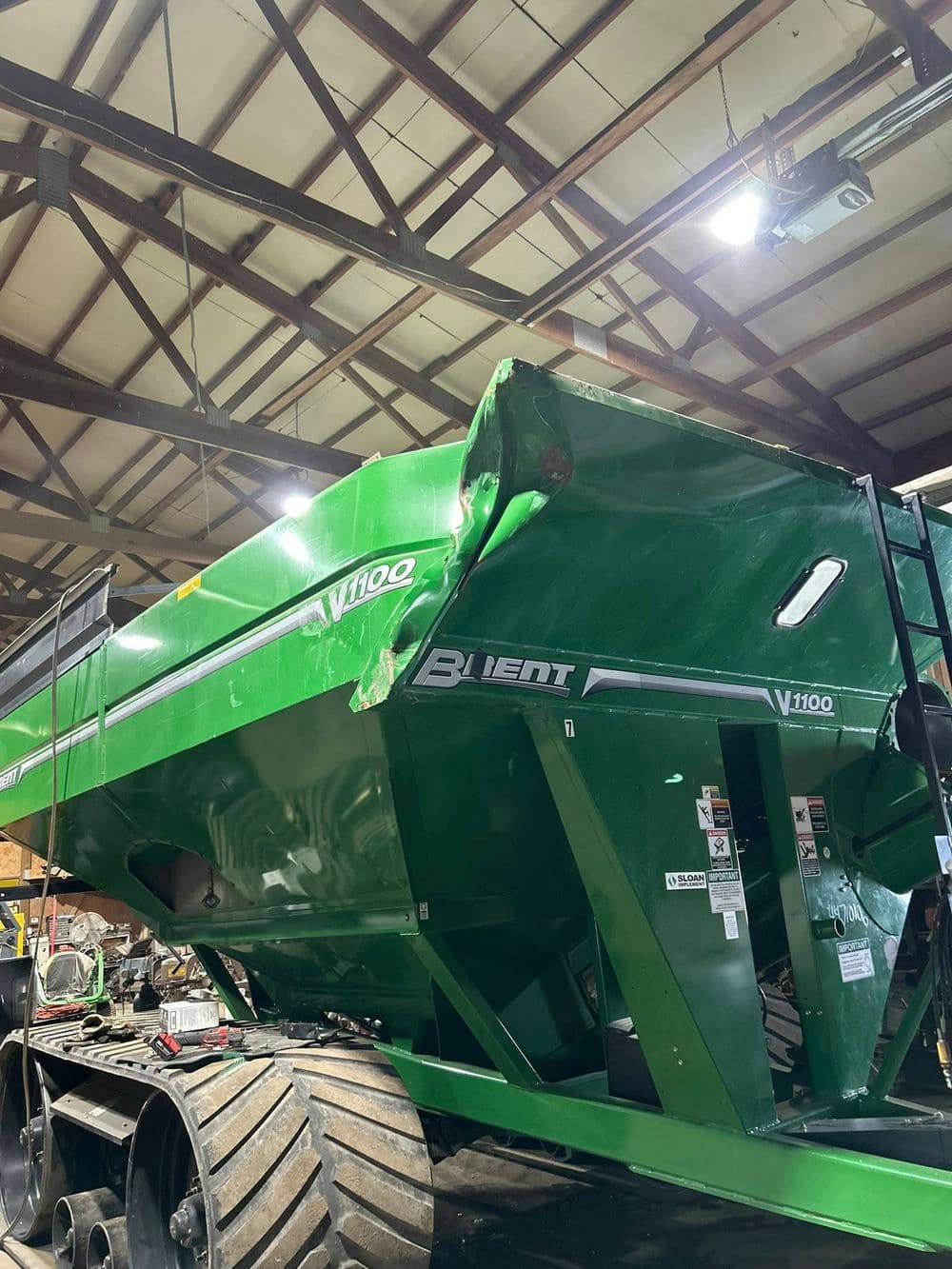 Green V1100 agricultural vehicle inside a warehouse with exposed beams.