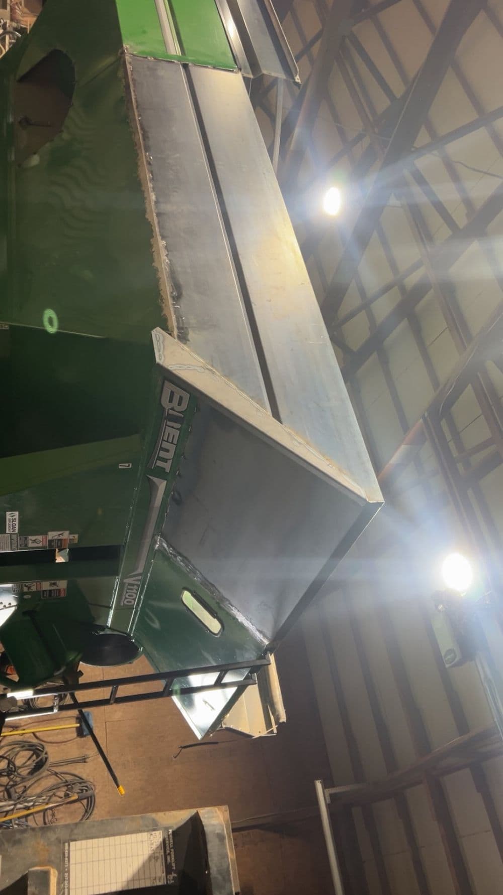 Green agricultural equipment in a well-lit barn setting with metal features.