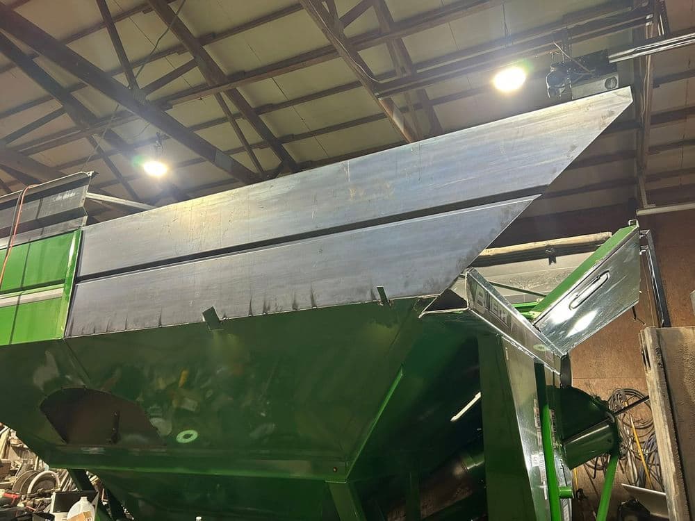 Metal agricultural equipment with a large angled hopper and industrial setting.