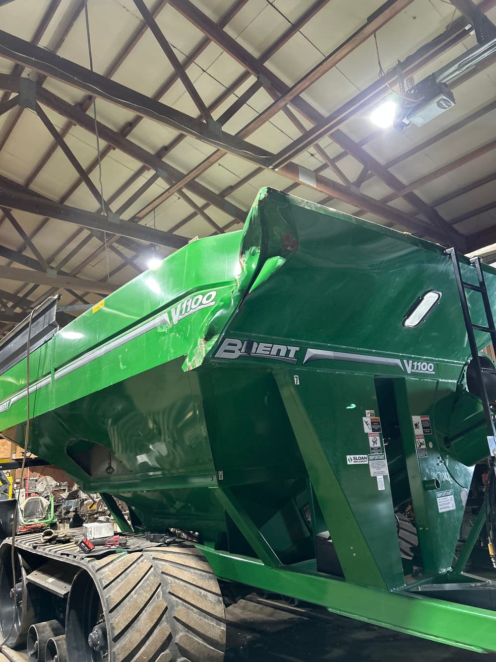Green V1100 agricultural trailer parked indoors, showcasing its robust design and features.
