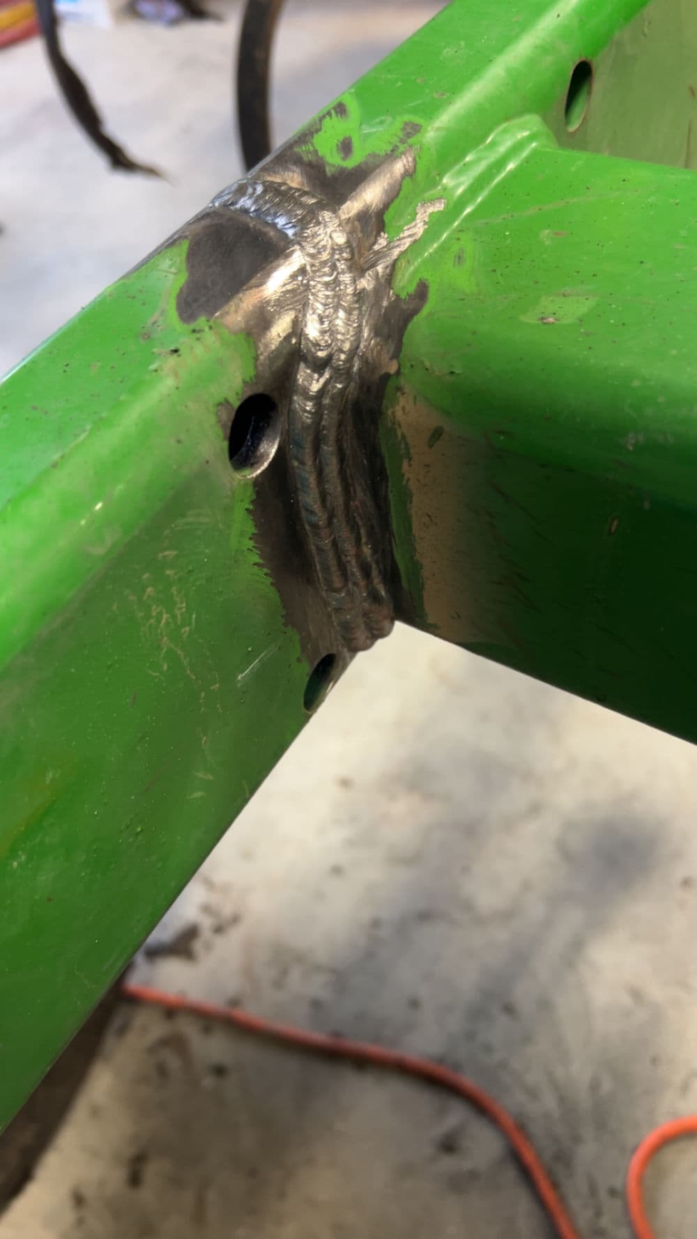Close-up of a green metal frame with a strong, glossy weld seam and drilling holes.
