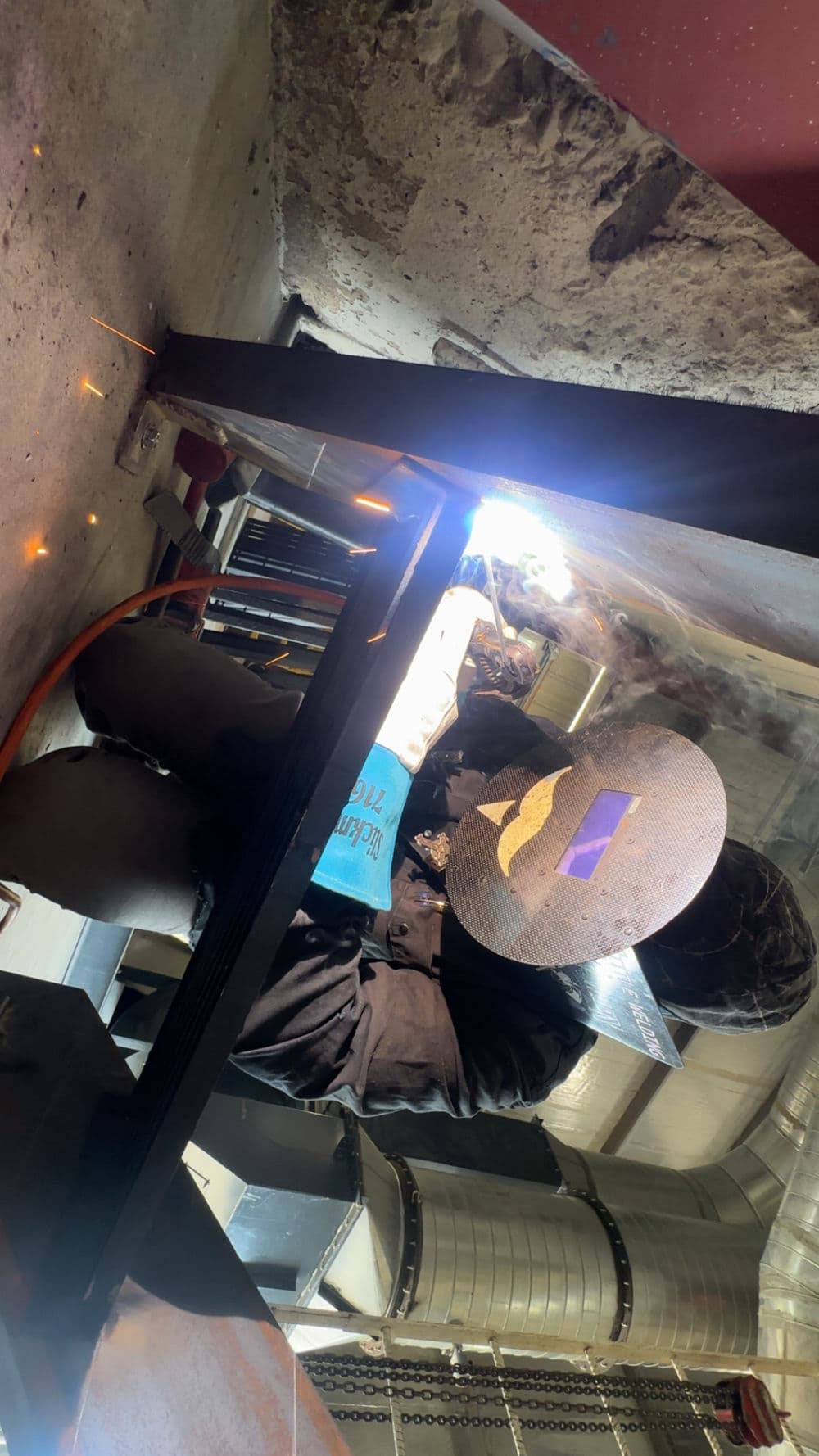 Welder working in a workshop, focused on a metal project with protective gear and sparks flying.