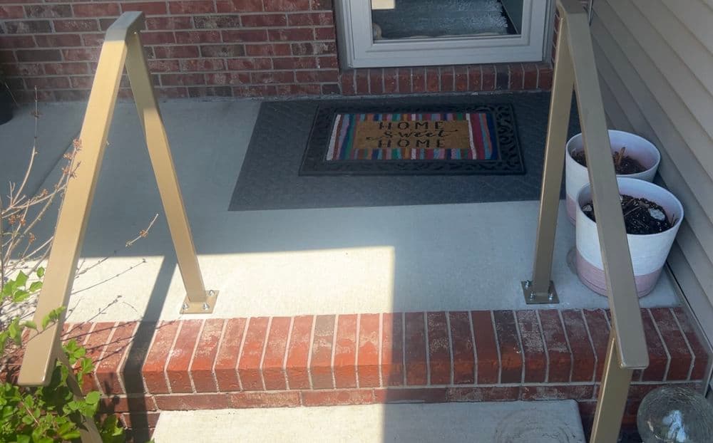 Handrails leading to a front porch with a welcome mat and potted plants. Safe entryway access.