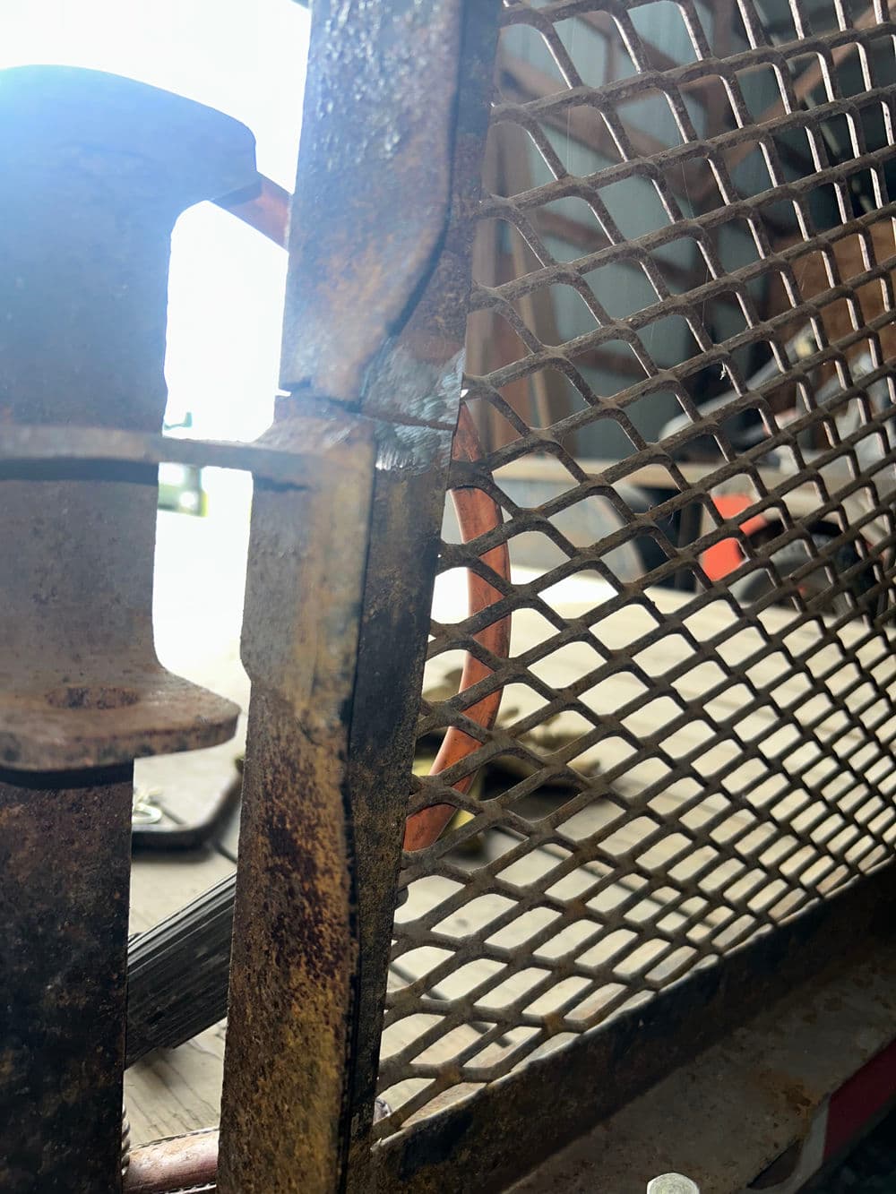 Rusty metal gate with a close-up of grid pattern and hinge detail in a workshop setting.