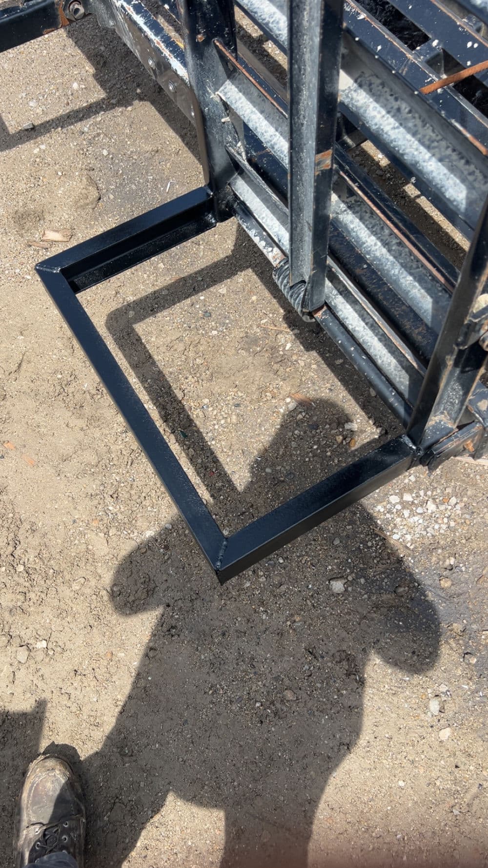 Heavy-duty metal frame on gravel surface with shadow from nearby equipment.