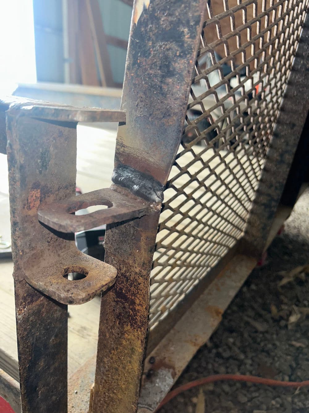 Rusty metal frame with mesh, showing detailed welding and joint close-up.